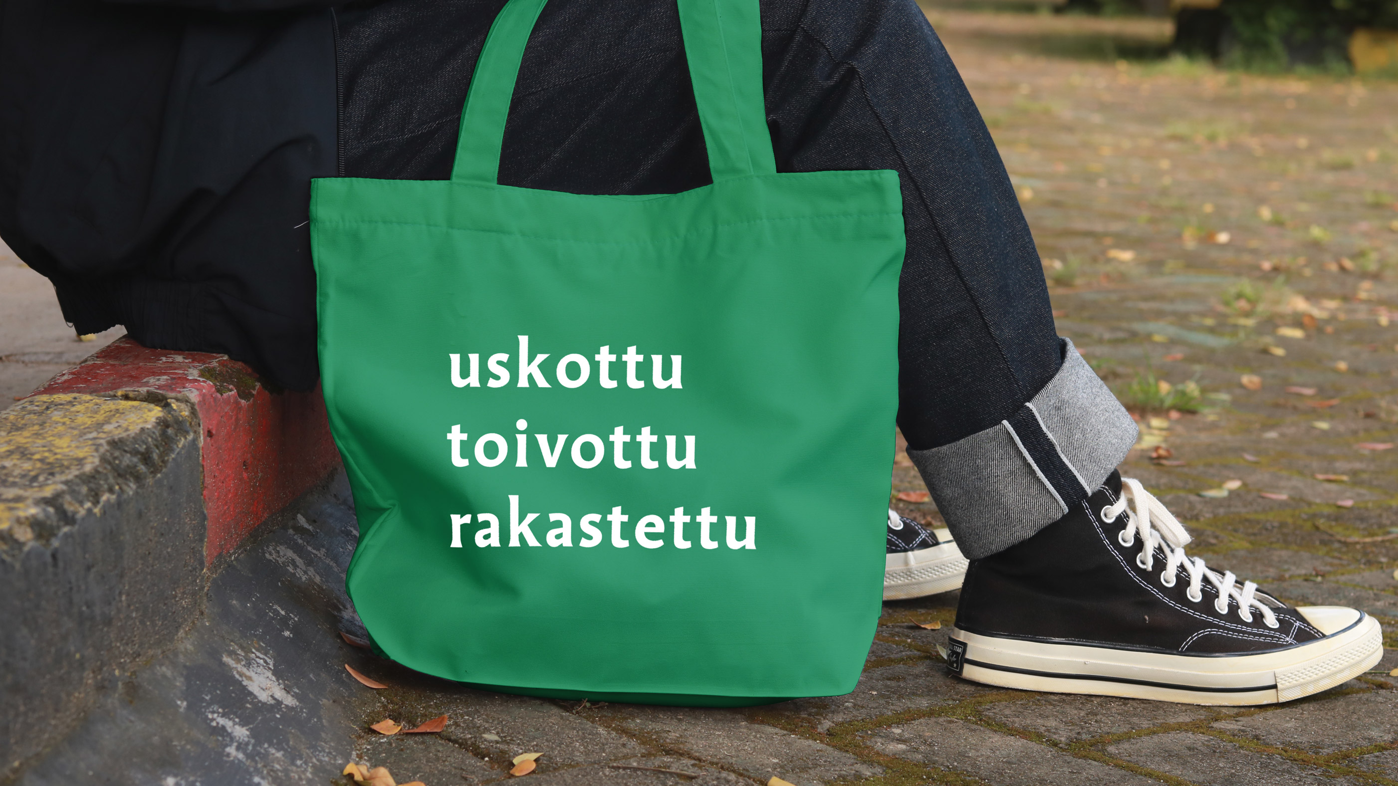 Vihreässä kangaskassissa teksti uskottu, toivottu, rakastettu. Vieressä näkyy tennarit.