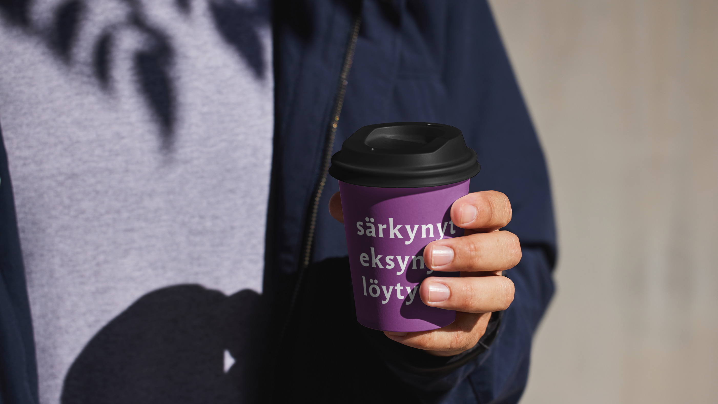 Henkilö pitelee kädessään violettia kahvikuppia.