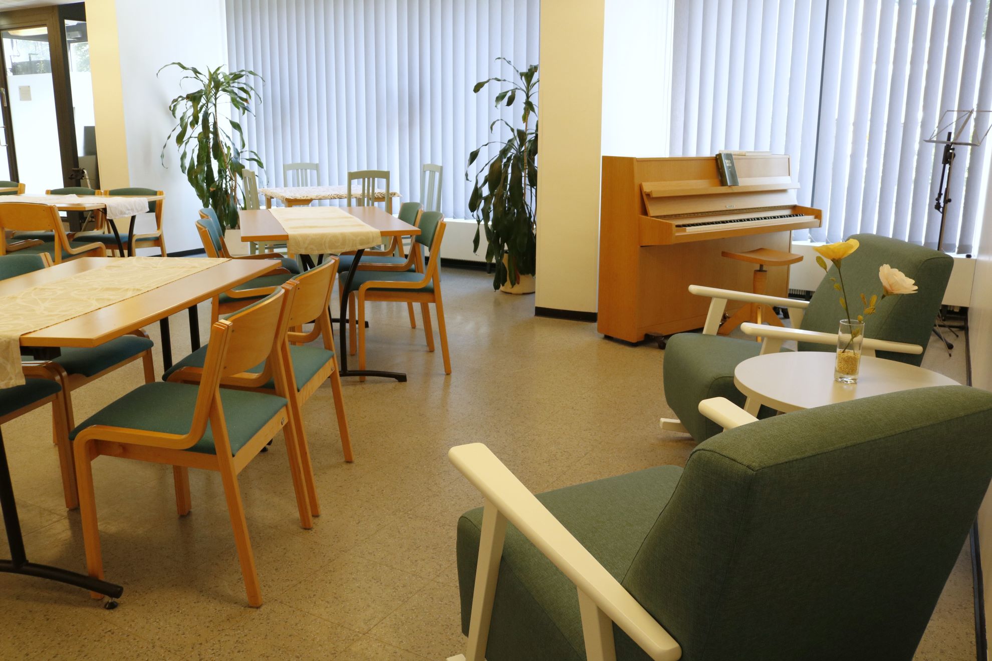 Seurakuntakodissa on pöytiä ja tuoleja, kaksi nojatuolia ja piano