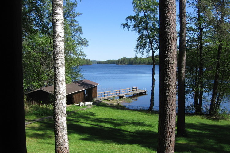 Kesäinen kuva rantasaunasta, järvi, puita ja nurmikkoa